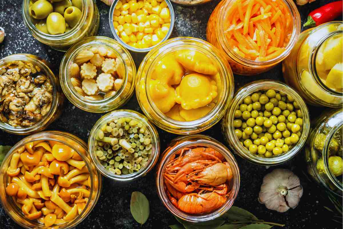tanti barattoli di vetro con dentro del cibo come piselli, gamberetti, carote e altre verdure